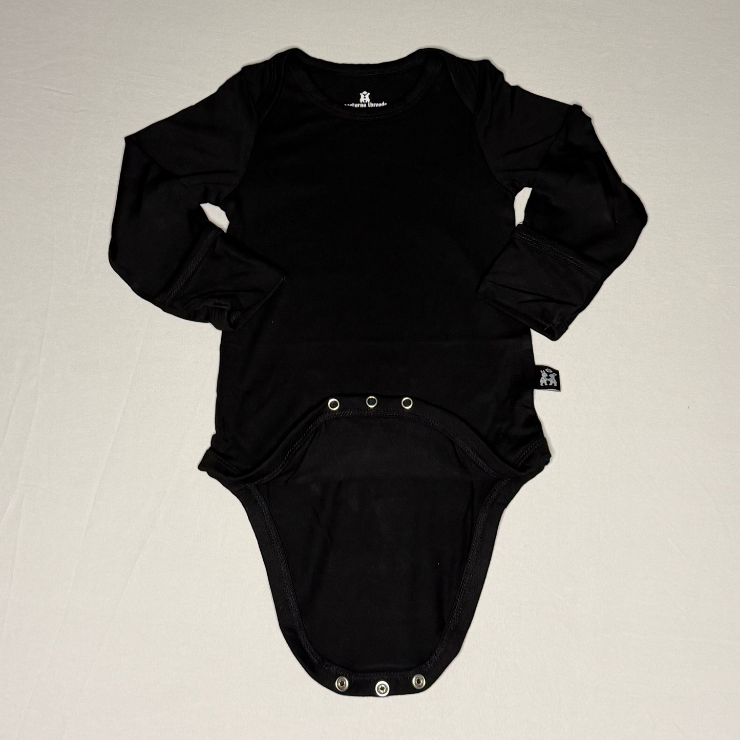 Black baby onesie with long sleeves on a beige background
